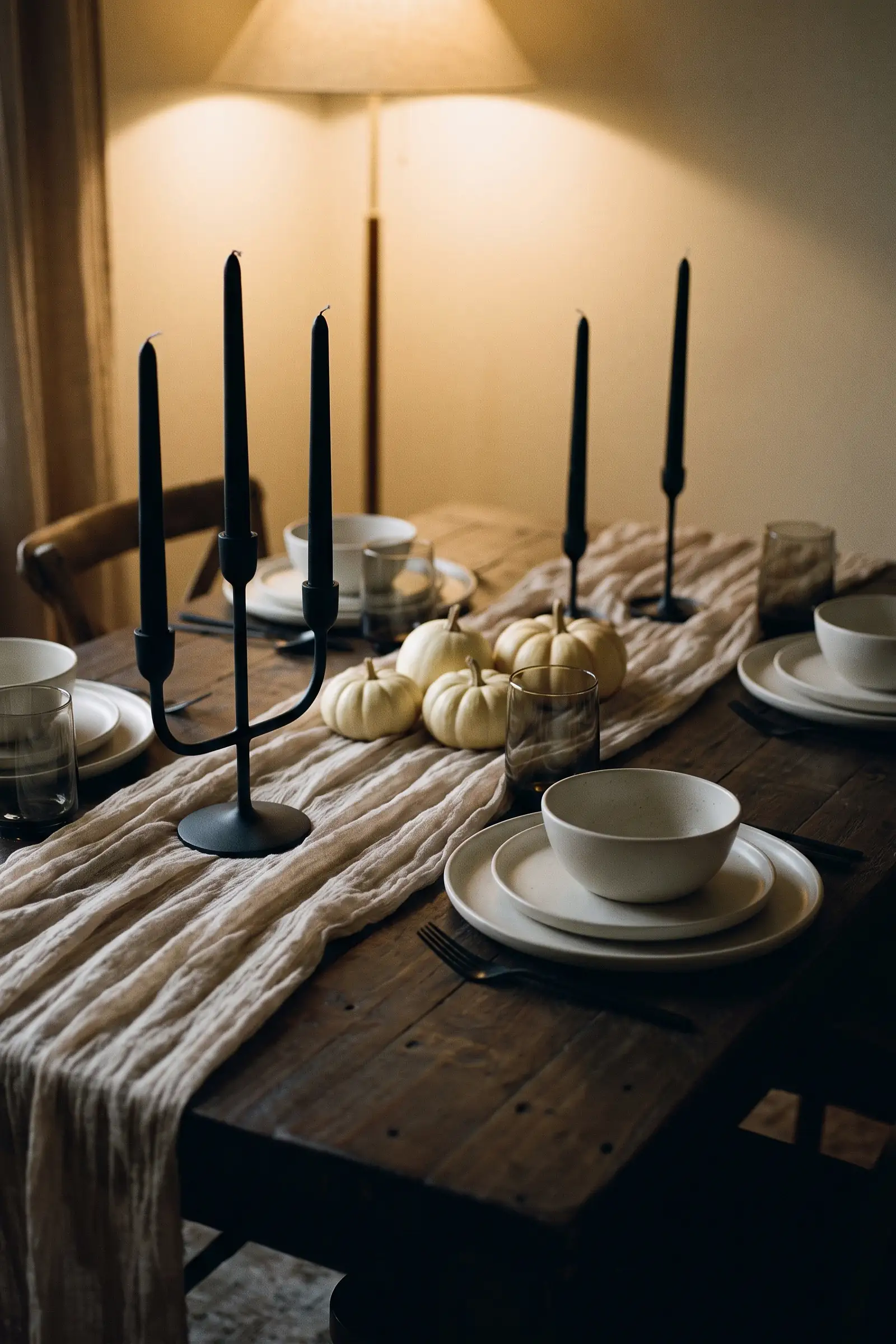 Neutral Halloween dining table with beige cheesecloth, black tapers, stoneware, and a sculptural candelabra