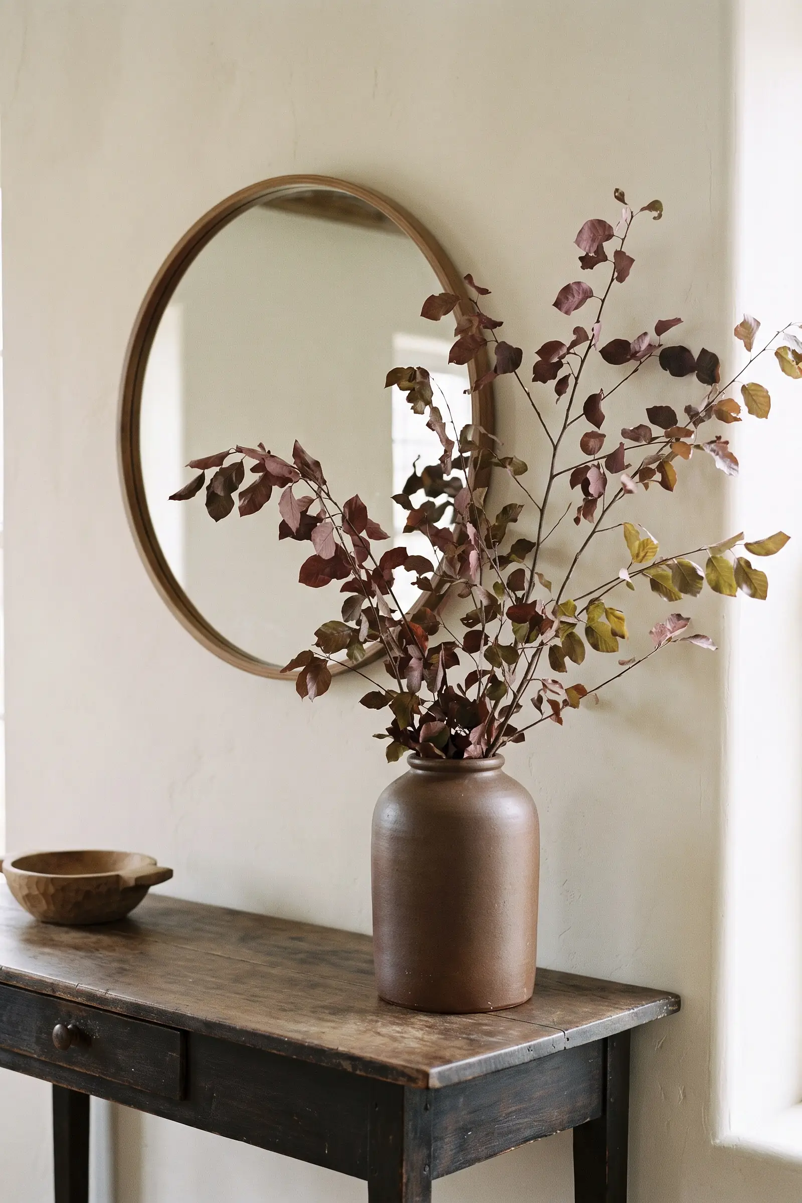 Rustic brown ceramic vase filled with tall muted autumn branches on a console
